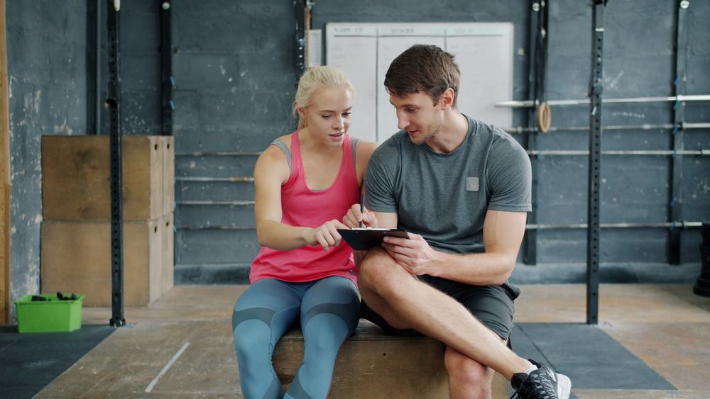Personal trainer and client reviewing a workout plan on a clipboard in a gym